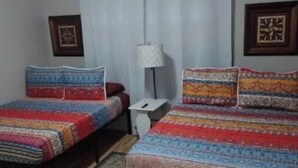A room with two beds, a small table, a lamp, and two framed pictures on the wall. - Close to Downtown, Restaurants, Markets , Events ,Beaches and Naval Base! (Pensacola)
