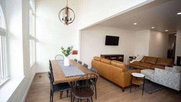 A spacious living area with a wooden dining table, leather sofas, and a TV mounted on the wall.