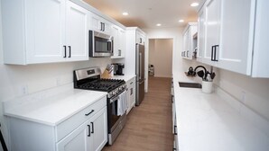 A modern kitchen with white cabinetry, stainless steel appliances, and a wooden floor.