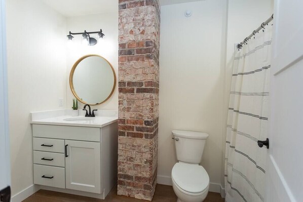 A bathroom with a white sink, a round mirror, a toilet, and a brick accent wall.