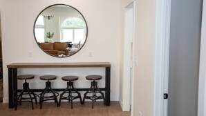 A dining area with a round mirror, a wooden bench, and four stools.