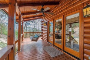 Une cabane en rondins avec une terrasse en bois, une chaise suspendue et de grandes fenêtres.