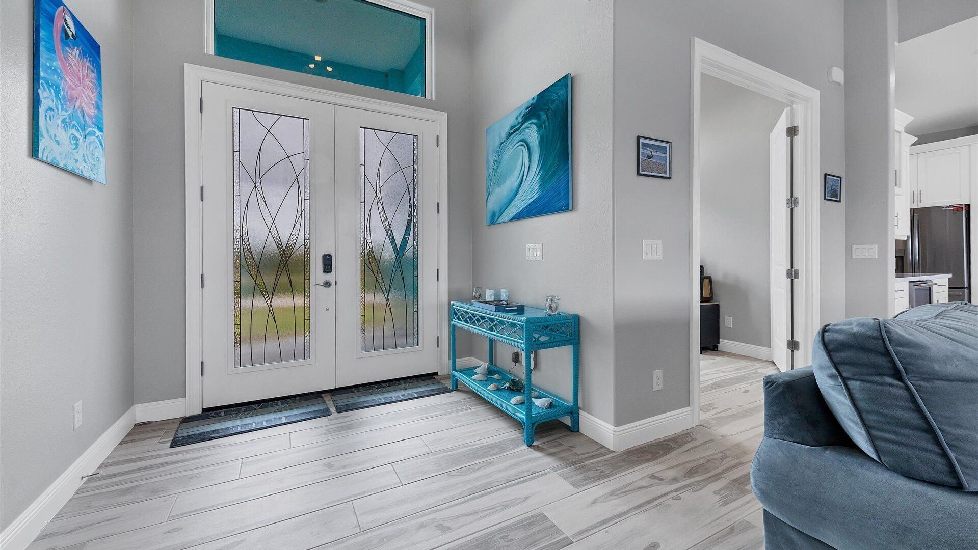 A modern entryway with a glass door, a blue console table, and a grey sofa.