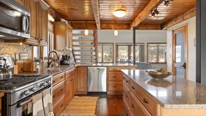 A kitchen with wooden cabinets, a stainless steel stove, and a large window providing a view of the outdoors.