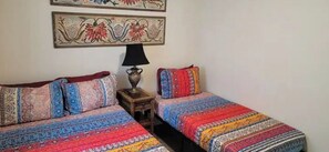 Une chambre avec deux lits, chacun agrémenté de draps à motifs et d’une table de chevet avec une lampe.