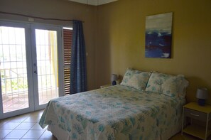 Une chambre à coucher comprenant un lit, une table de chevet, une lampe, un tableau et une porte-fenêtre coulissante donnant sur un espace extérieur.