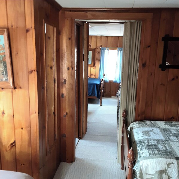 A wooden room with a bed, a door leading to another room, and a window with curtains.