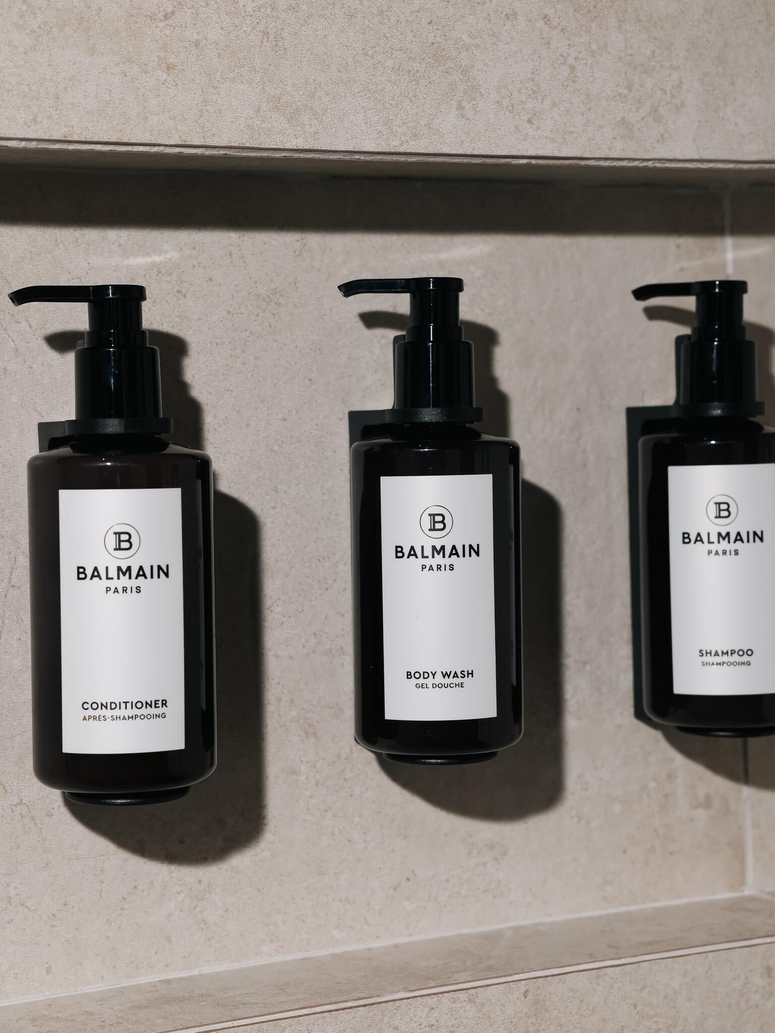 Tres botellas de Balmain Paris sobre una pared.