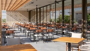 Un café moderno al aire libre con numerosas mesas y sillas, ventanas amplias y una estructura de techo de madera.