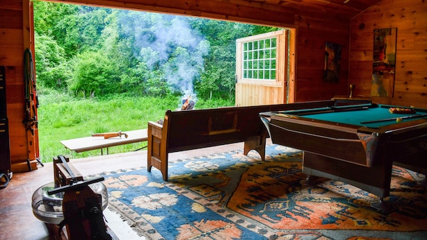 Eine Holzhütte mit Billardtisch, einer Bank und Blick auf einen Wald durch eine Tür.