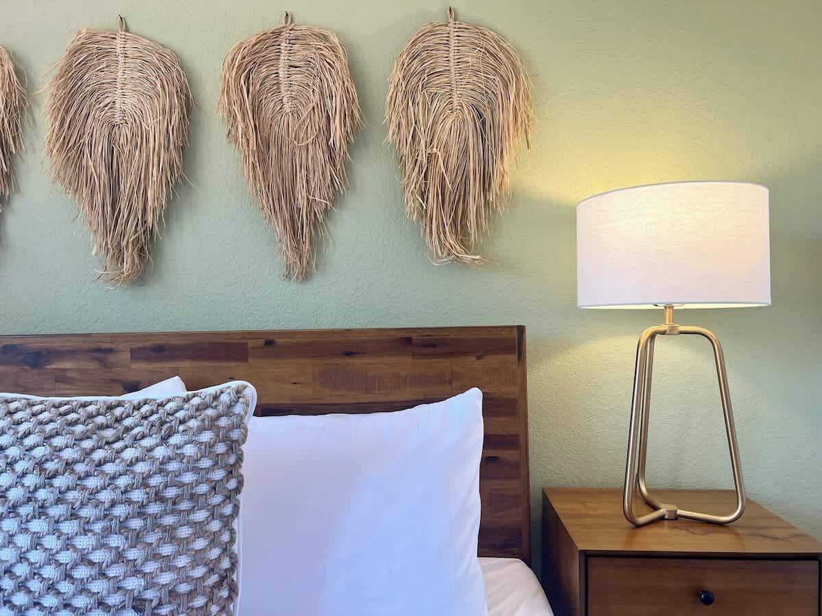 Una cama con almohadas blancas y estampadas, un cabecero de madera y una mesita de noche con una lámpara.