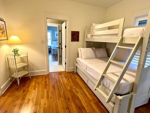 A room with a bunk bed, a small table with a lamp, and a door leading to another room.