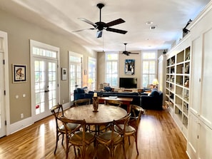 A spacious living room with a wooden dining table, blue sofas, and a ceiling fan.