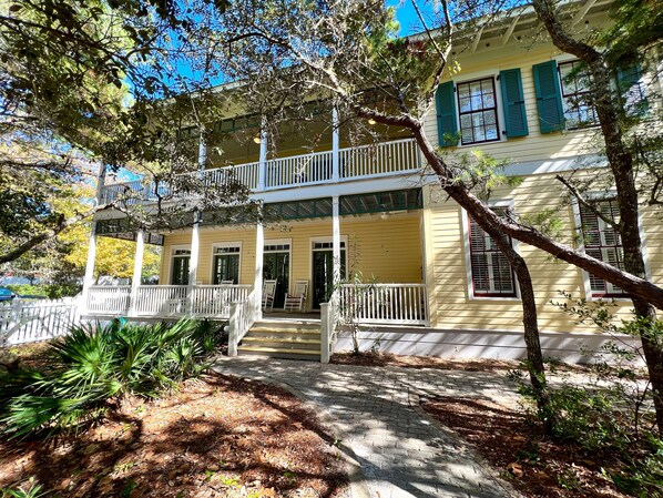 A two-story building with a balcony, a porch, and a brick pathway leading to the entrance.