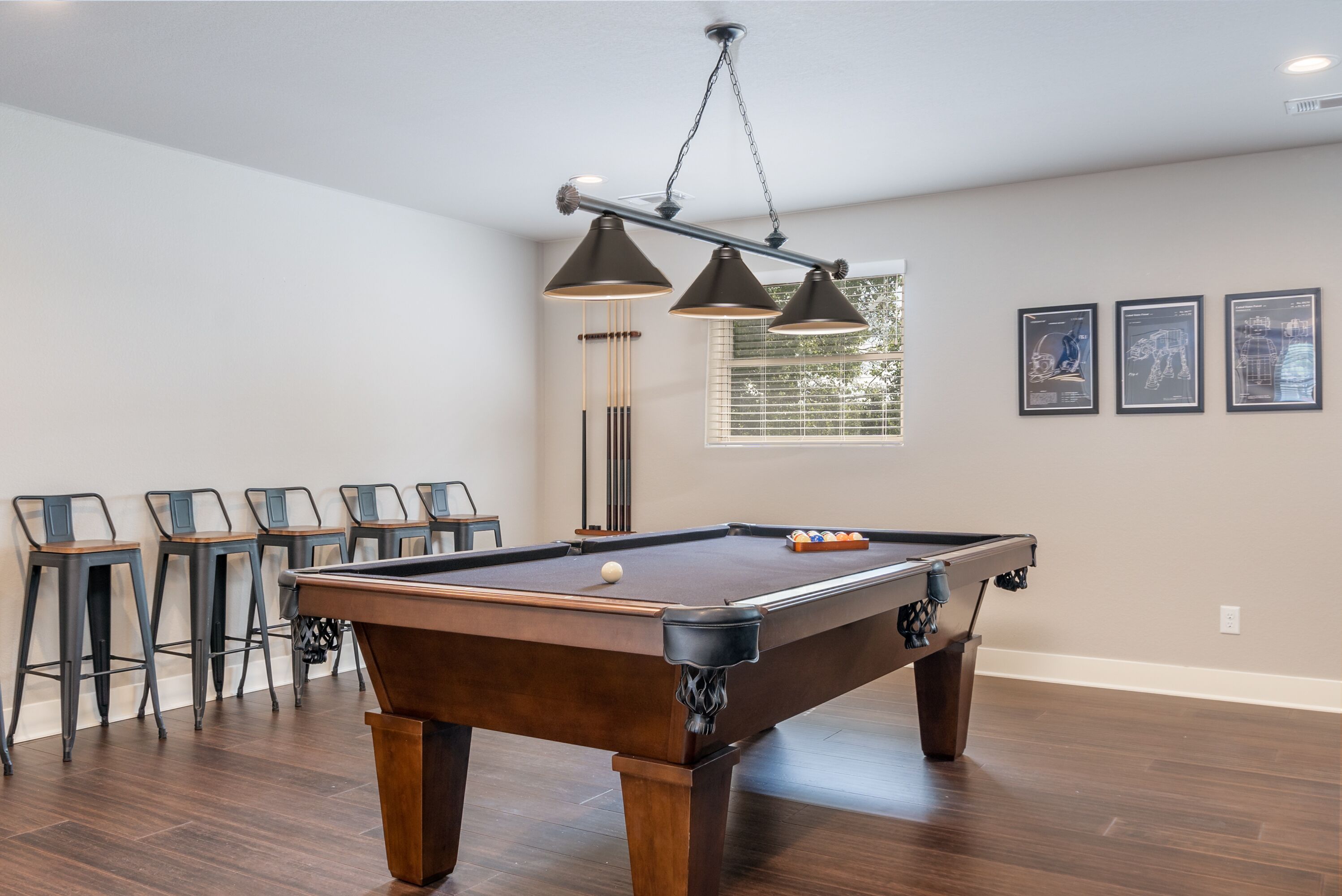 Een pooltafel met hanglamp, barstoelen en kunstwerken in een lijst aan de muur.