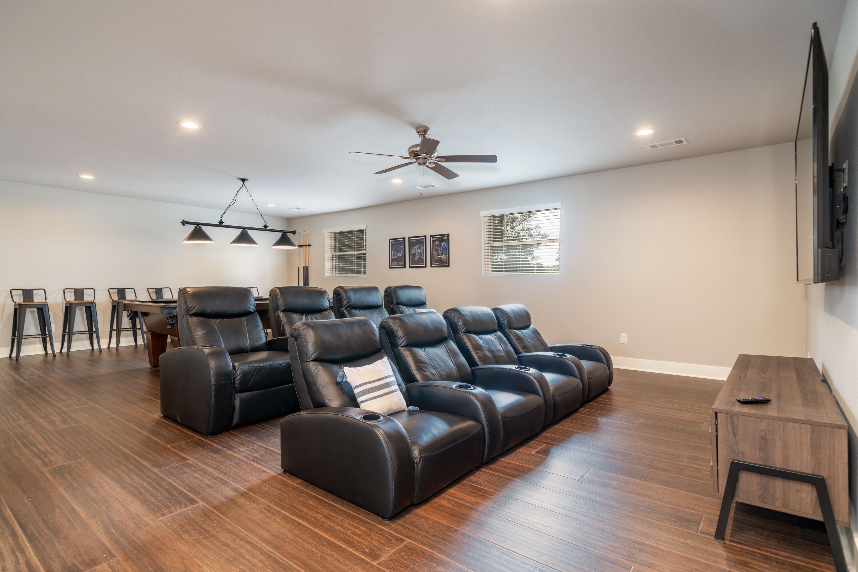 A spacious living room with a large black leather sofa, a ceiling fan, recessed lighting, and a wooden coffee table.