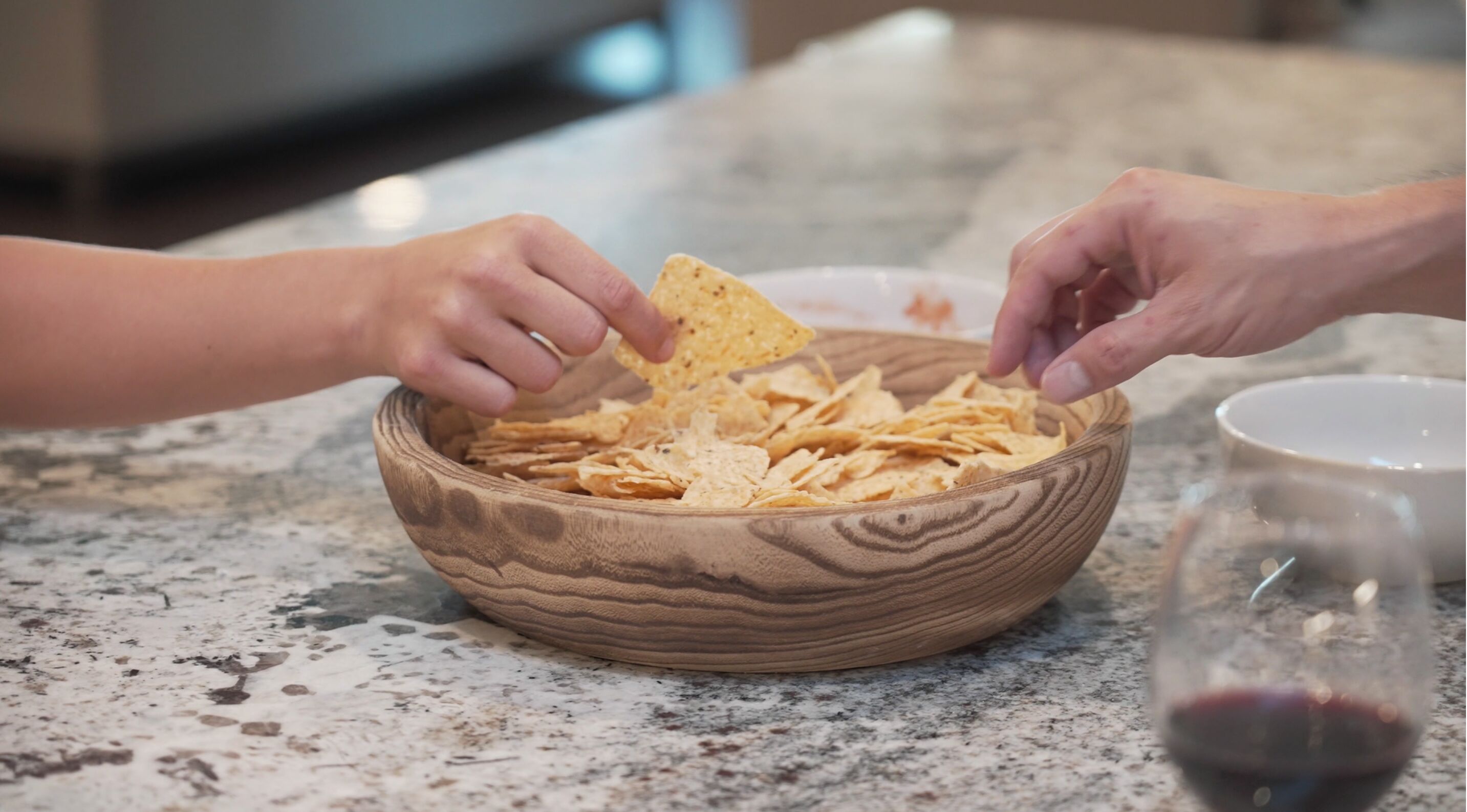 A wooden bowl filled with chips on a granite countertop.