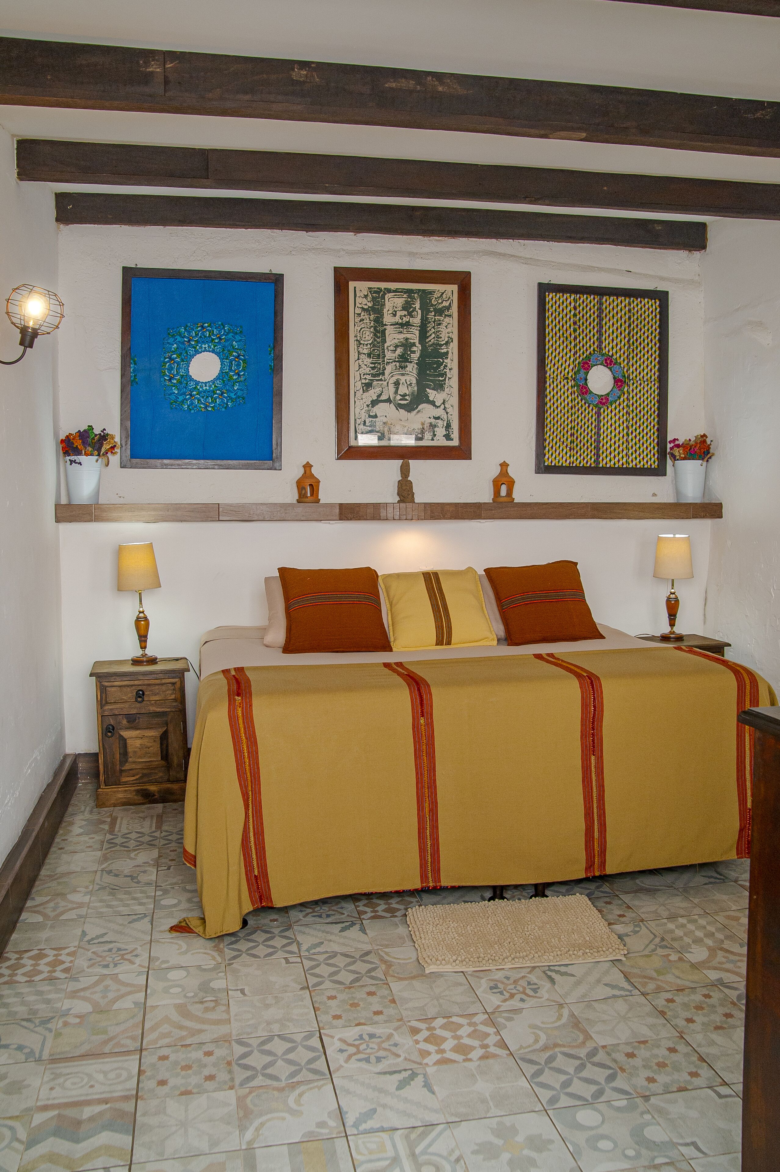 Ein Schlafzimmer mit einem Bett, zwei Nachttischen mit Lampen, einem gemusterten Teppich und Wandbildern.