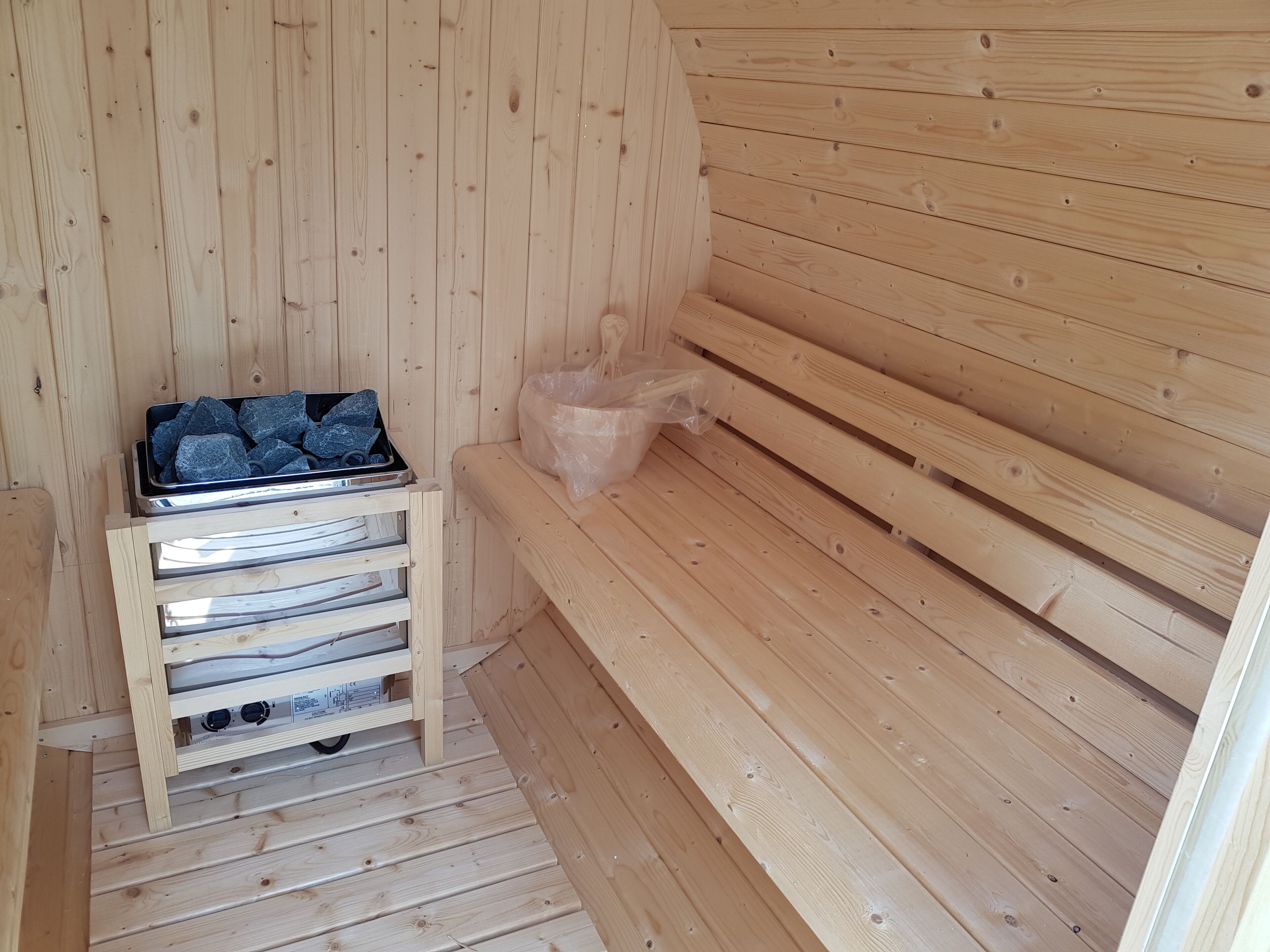 Eine Holzsauna mit Bänken und einem Metallbehälter für Steine.