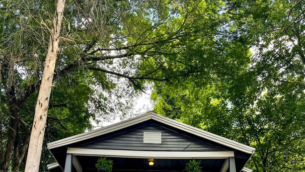 A building with a porch, a staircase leading up to the entrance, and a surrounding landscape with trees and grass. - NEW! Modern & Cozy close to Downtown Attractions! (Hot Springs)