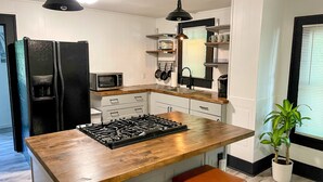 A modern kitchen with a central island, wooden countertops, a gas stove, a microwave, and a refrigerator. There are two pendant lights above the island and a potted plant on the right. - NEW! Modern & Cozy close to Downtown Attractions! (Hot Springs)