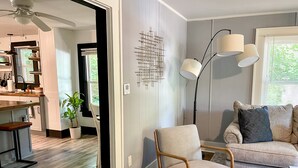 A modern living room with a grey sofa, a wooden chair, and a dining area with a kitchen counter. - NEW! Modern & Cozy close to Downtown Attractions! (Hot Springs)