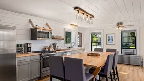 A modern kitchen with stainless steel appliances, a wooden dining table, and a large window providing a view of the outdoors. - The Homestead - Walk to village, bring the pup! (Johnson)