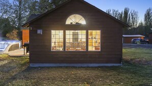 Una piccola baita di legno con un'ampia finestra, un'area patio e un garage visibile.