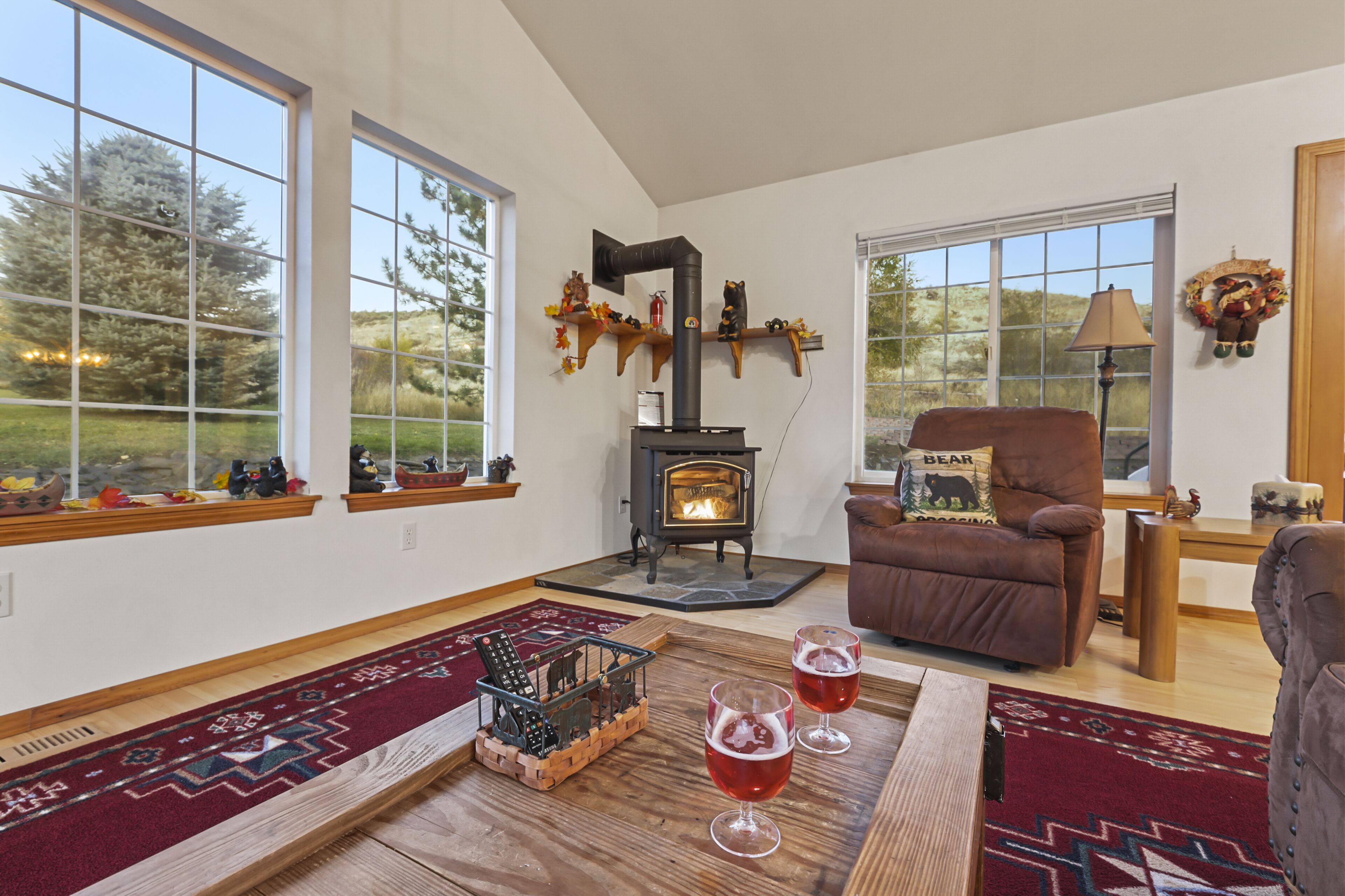 Una sala de estar acogedora con chimenea, ventanas amplias, un sillón de cuero marrón y una mesa de centro de madera con vasos.