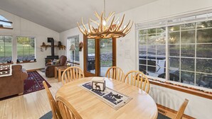 Un'ampia sala da pranzo con un tavolo e sedie in legno, un lampadario e grandi finestre che offrono vista sull'esterno.