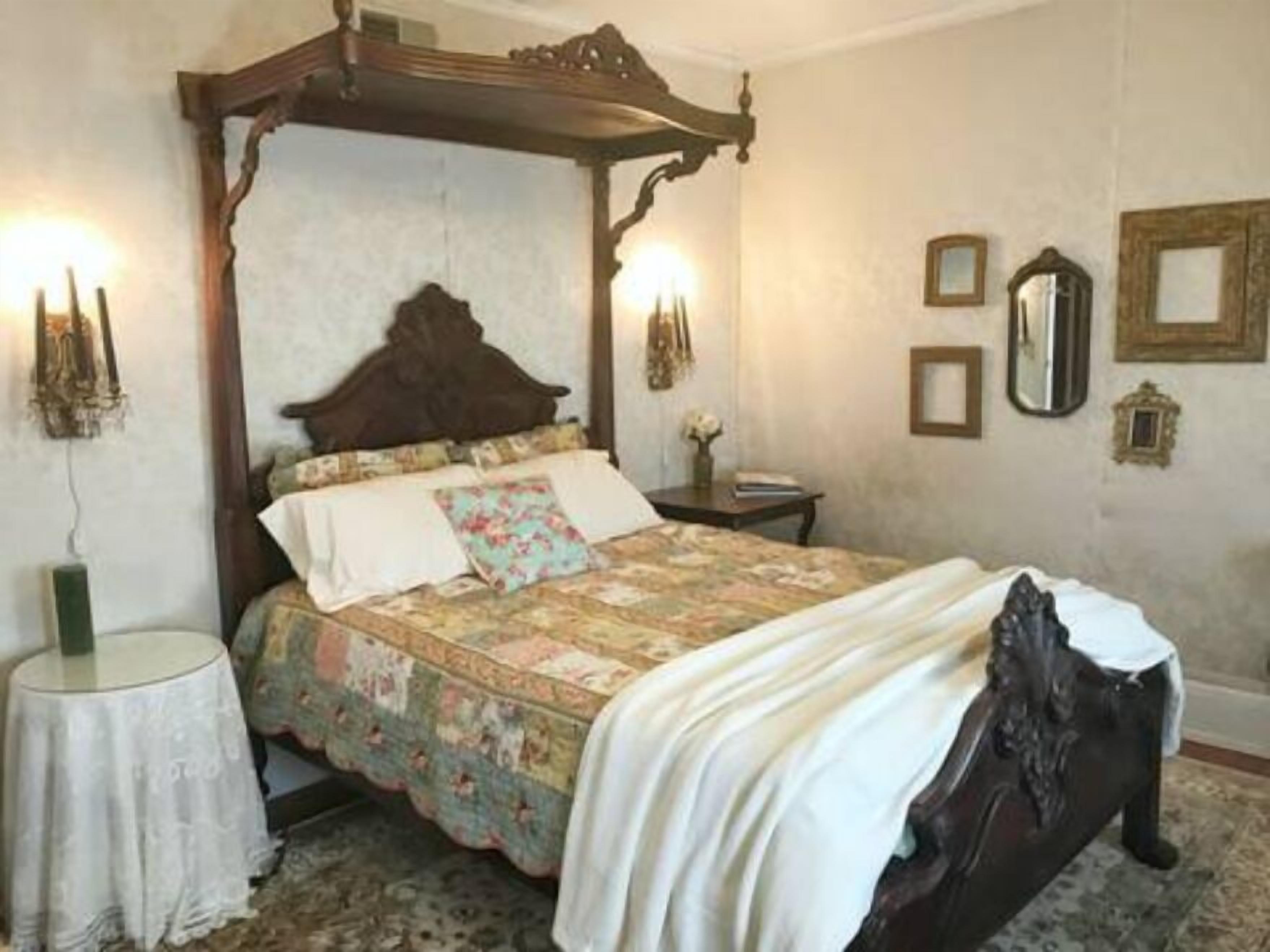 Un lit à baldaquin avec une couvre-lit à motifs floraux, une petite table de chevet ornée d’un vase et des miroirs fixés au mur.