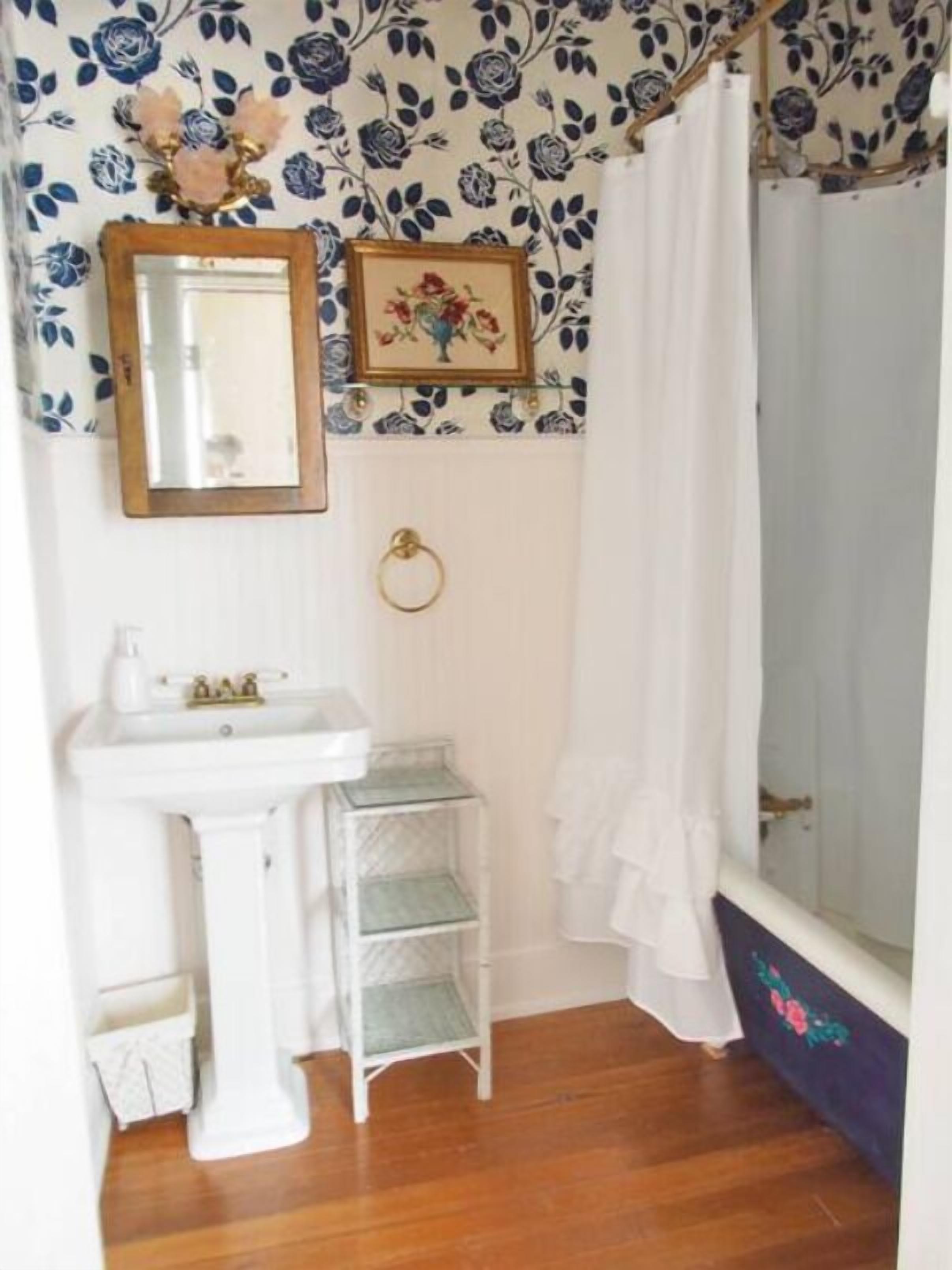 A bathroom with a white sink, a mirror, a framed floral picture, a ring on the wall, and a shower curtain.