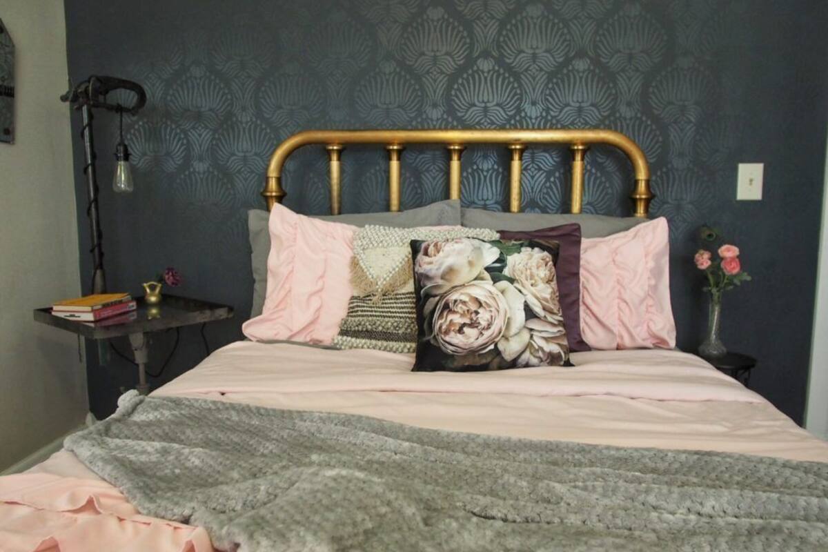 A bed with a gold headboard, pink and gray bedding, and decorative pillows.