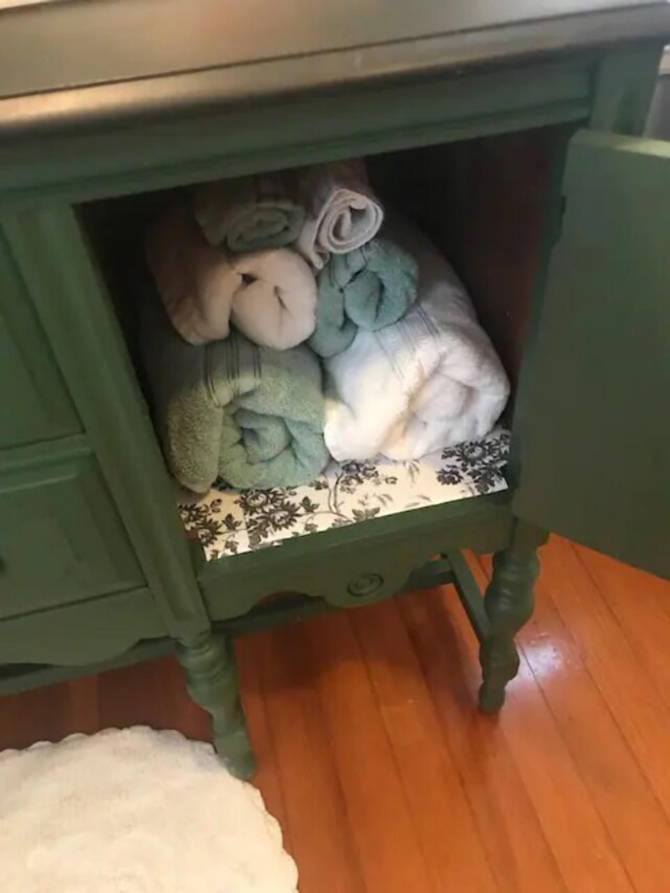 A green wooden dresser with a drawer containing rolled towels.
