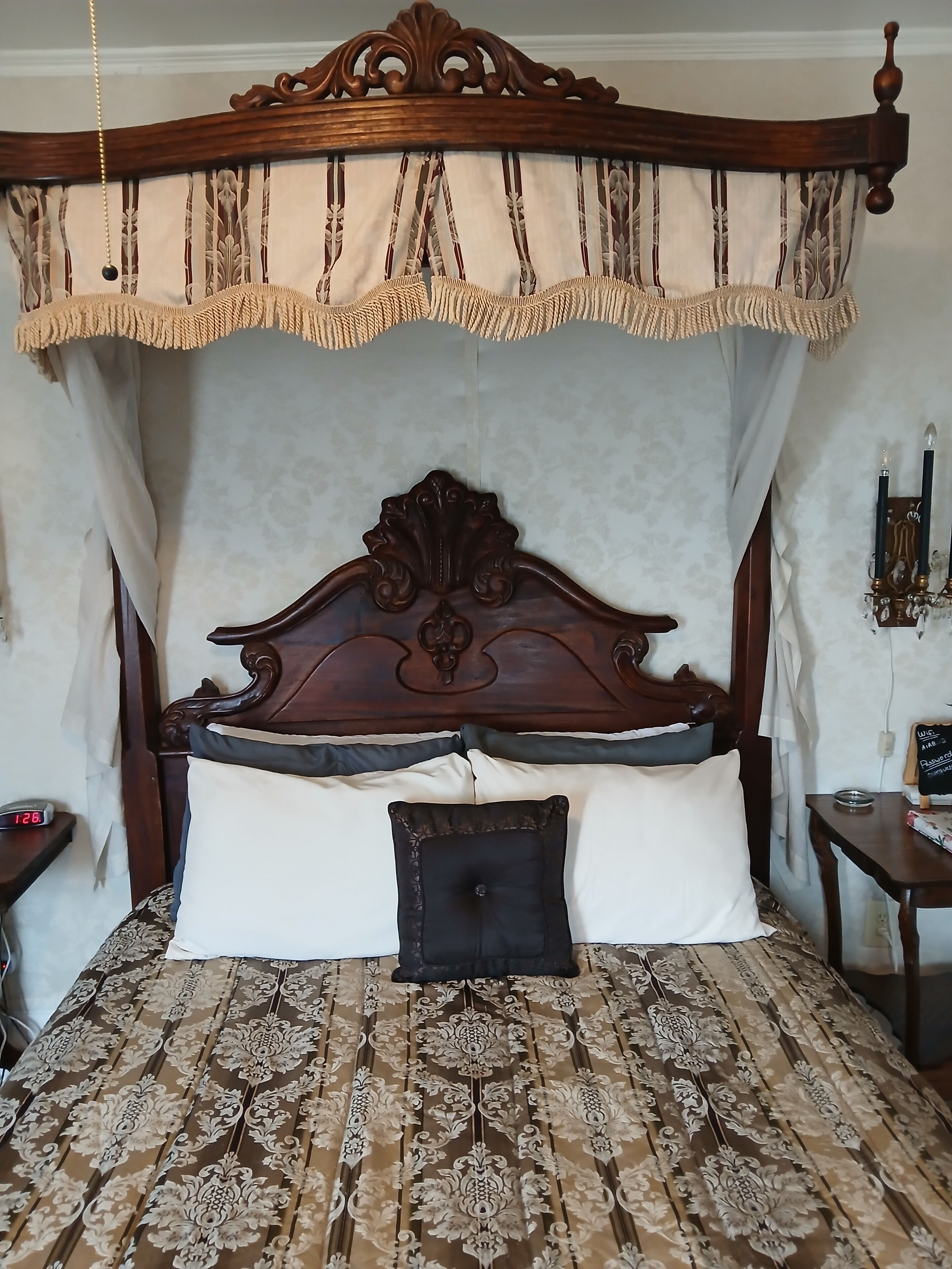 Un dormitorio con cama de dosel de madera, colcha estampada y mesita de noche con un reloj.