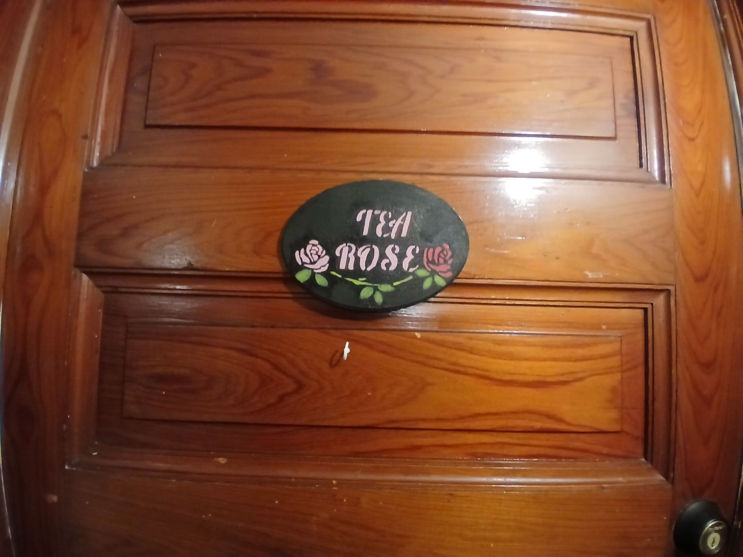 Eine Holztür mit einem Schild, auf dem 'TEA ROSE' steht.