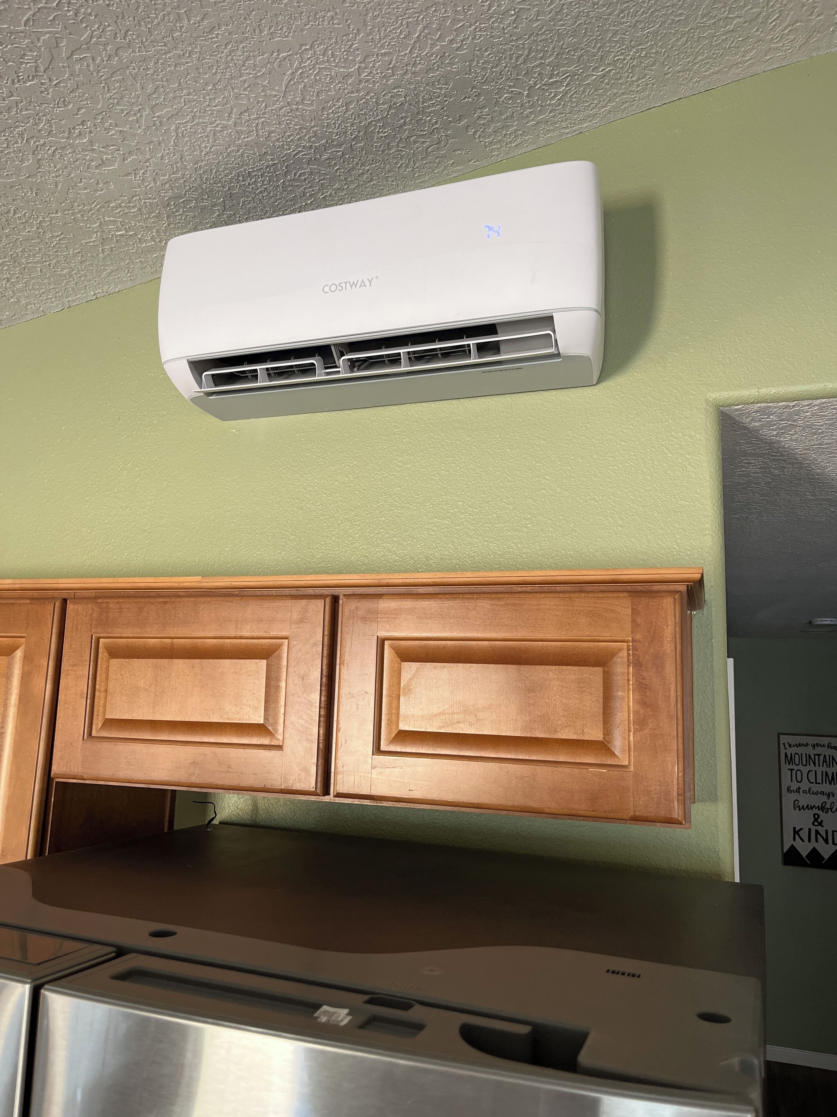 A kitchen with a built-in stainless steel refrigerator, wooden cabinets, and a wall-mounted air conditioner.
