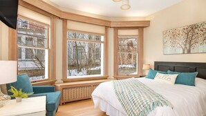 Une chambre avec un grand lit, une vue sur l’extérieur, un coin fenêtre et un tableau au mur.