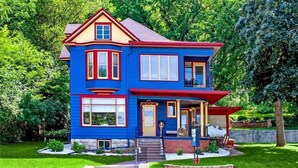 Une maison à deux étages avec un toit rouge, un revêtement bleu et une véranda à l’avant.