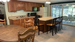 A kitchen with wooden cabinets, a central island, a dining table with chairs, and a large window with a view of the outdoors. - Cozy Lake House: Ark Encounter, Kincaid Lake, KY- Fishing, Scenic Get-Away (Falmouth)