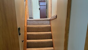 A carpeted staircase with wooden handrails and a door on the left. - Cozy Lake House: Ark Encounter, Kincaid Lake, KY- Fishing, Scenic Get-Away (Falmouth)
