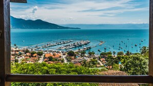 A coastal town with a marina, houses with red roofs, and a mountain in the background. - Casa Tiffany - Ilhabela (Ilhabela)