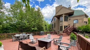 A deck with outdoor furniture, a grill, and a house with a staircase.