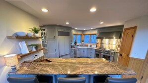 A kitchen with a granite island, bar stools, and a view of the outdoors.