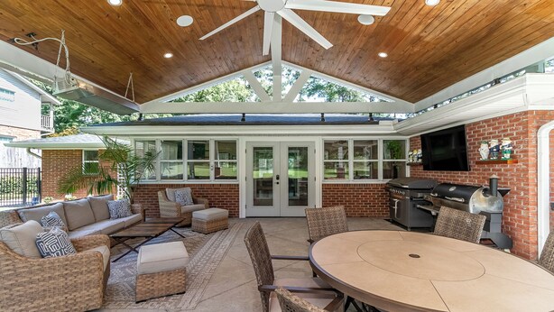 Une terrasse extérieure aménagée avec des meubles en osier, une table ronde et un espace barbecue.