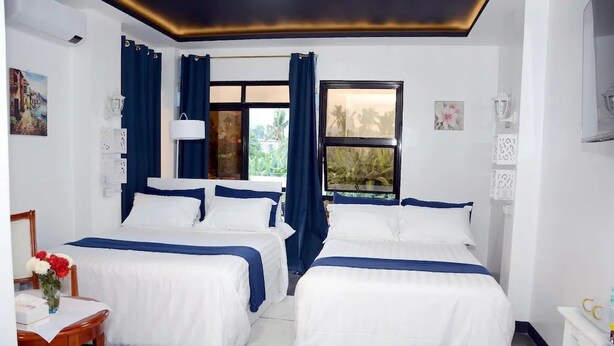 A hotel room with two beds, a desk, a chair, and a window with curtains. - QUEEN SUITE ROOM R#4 (Sogod, Southern Leyte)