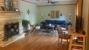 Un salon avec une cheminée, un canapé bleu, une table basse en bois et un téléviseur posé sur un meuble.