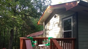 Une terrasse en bois avec une rambarde, une table et deux chaises vertes.