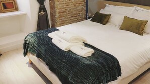 Een moderne slaapkamer met een bakstenen muur, een groot bed met witte lakens en een donkergroene plaid.