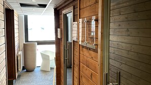 Un couloir moderne avec un lambris en bois, une porte en verre et un coin salon comprenant une chaise et une table blanches.